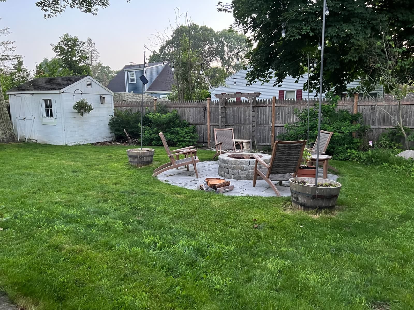 Backyard patio with chairs, fire pit, string lights, lawn, and shed.