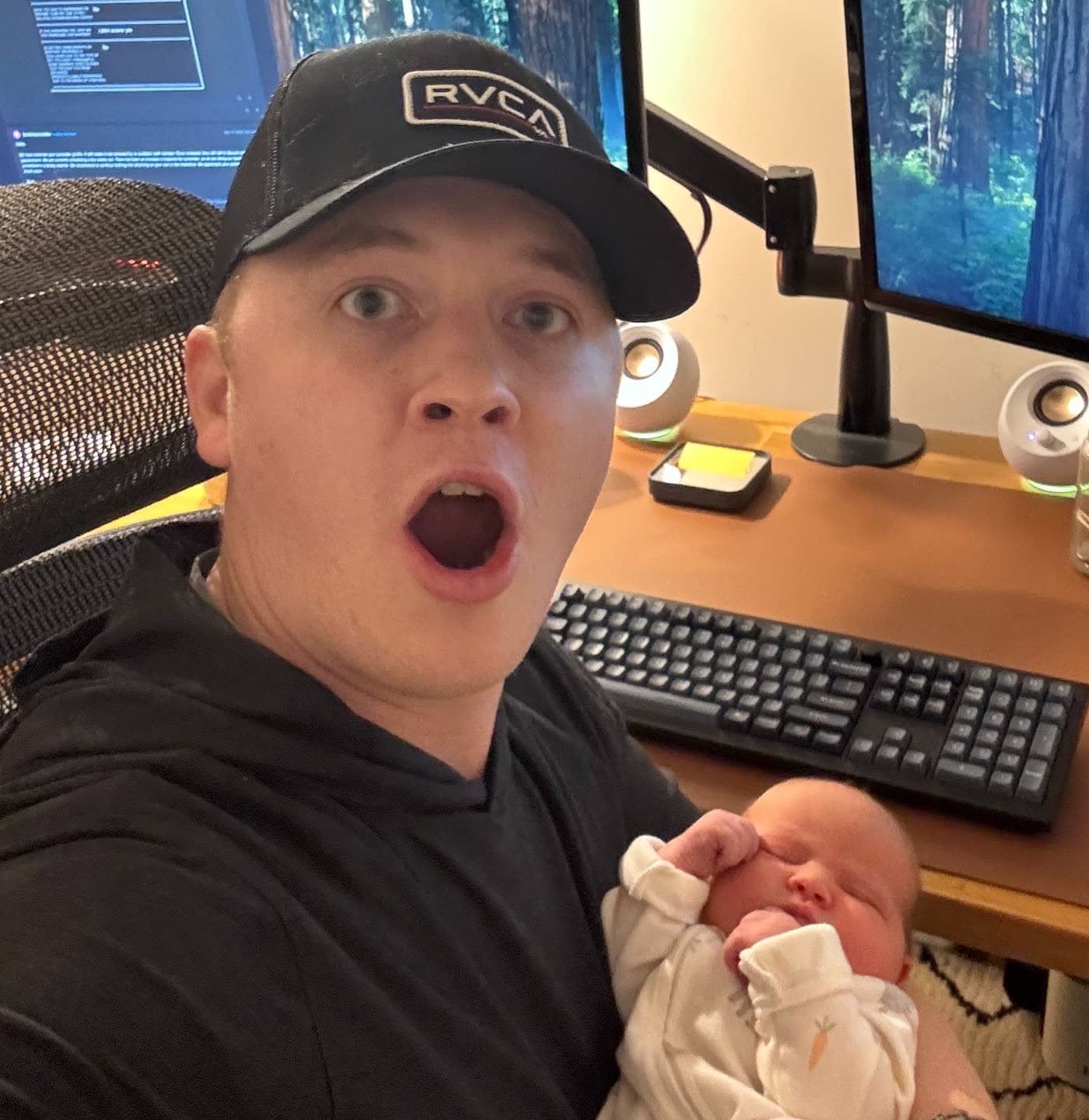 Mike holding newborn daughter Mia at a home desk setup.